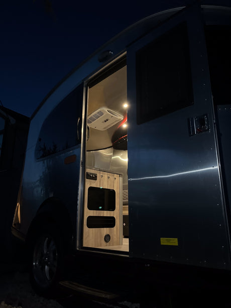 Silver RV rental at night, door open to its illuminated interior. A cozy travel trailer awaits.