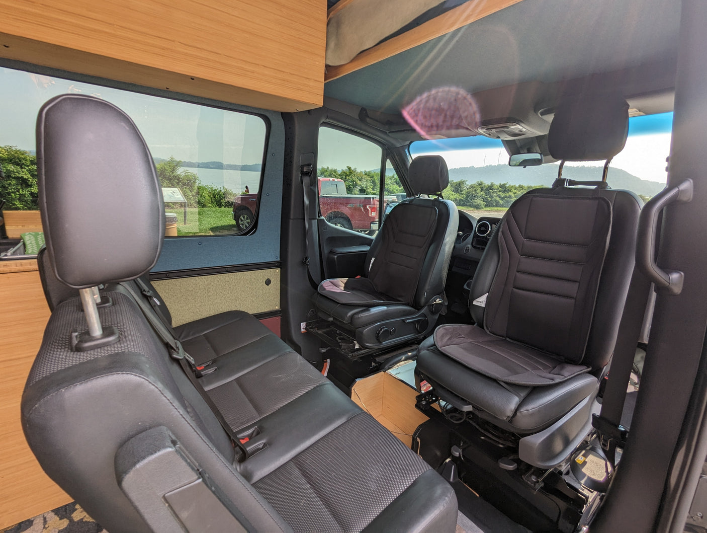 RV rental: Inside a comfortable camper van, featuring swiveling front seats, a rear bench, and scenic window views.
