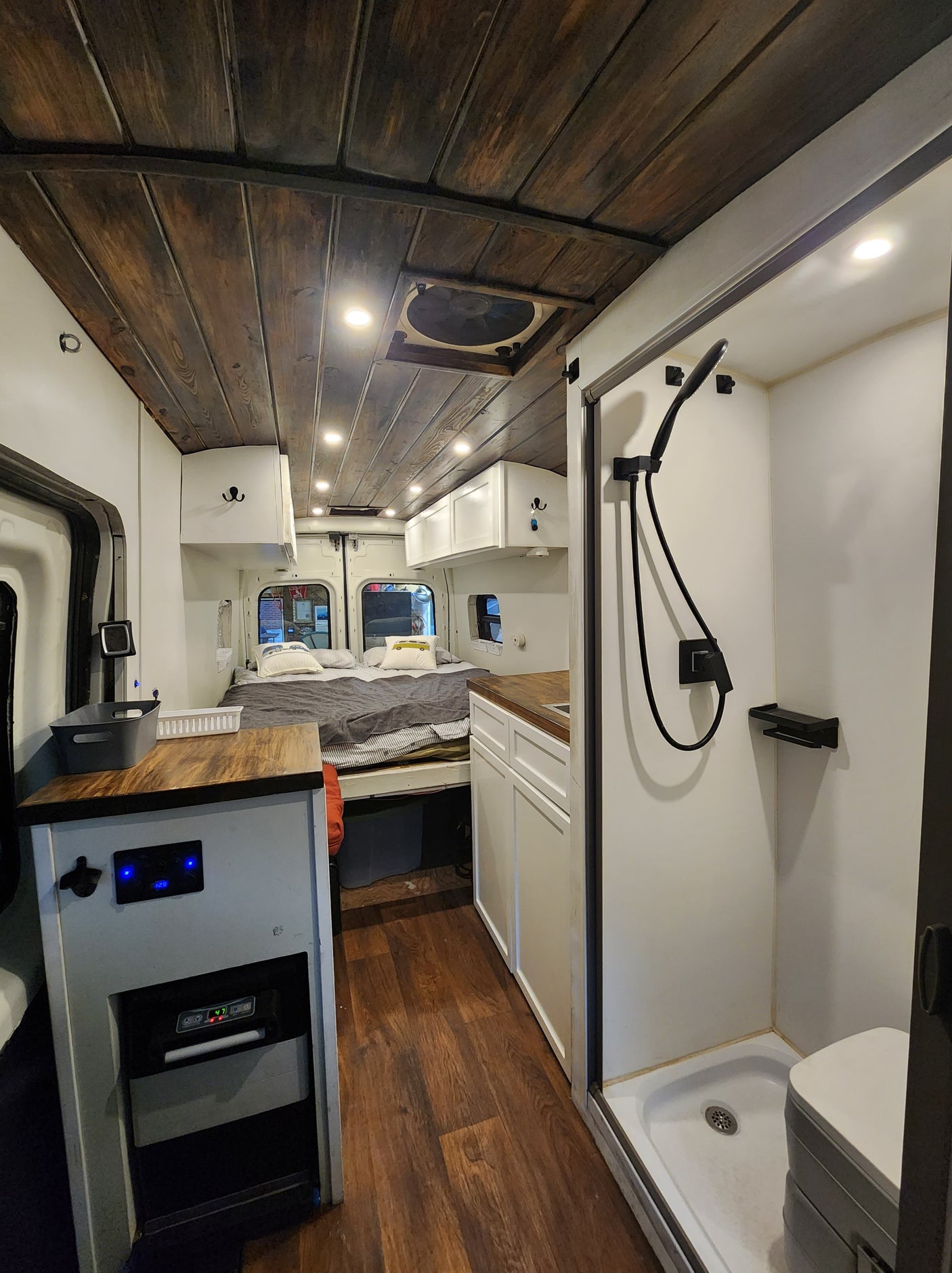 This RV rental showcases a thoughtfully designed camper van interior with a cozy bed, full shower, and modern kitchen setup.