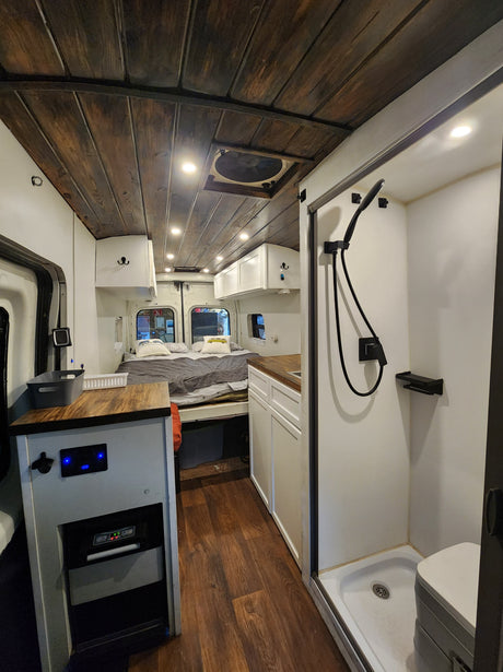 This RV rental showcases a thoughtfully designed camper van interior with a cozy bed, full shower, and modern kitchen setup.