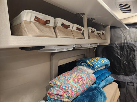 Cozy RV rental interior with organized storage bins, colorful blankets, and under-shelf mesh baskets.