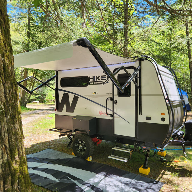 A Winnebago Hike travel trailer, ideal for an RV rental, parked under a canopy of trees at a serene campsite.