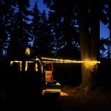 Cozy night setup with an RV rental. String lights illuminate the van's interior and a tree in the dark forest campsite.