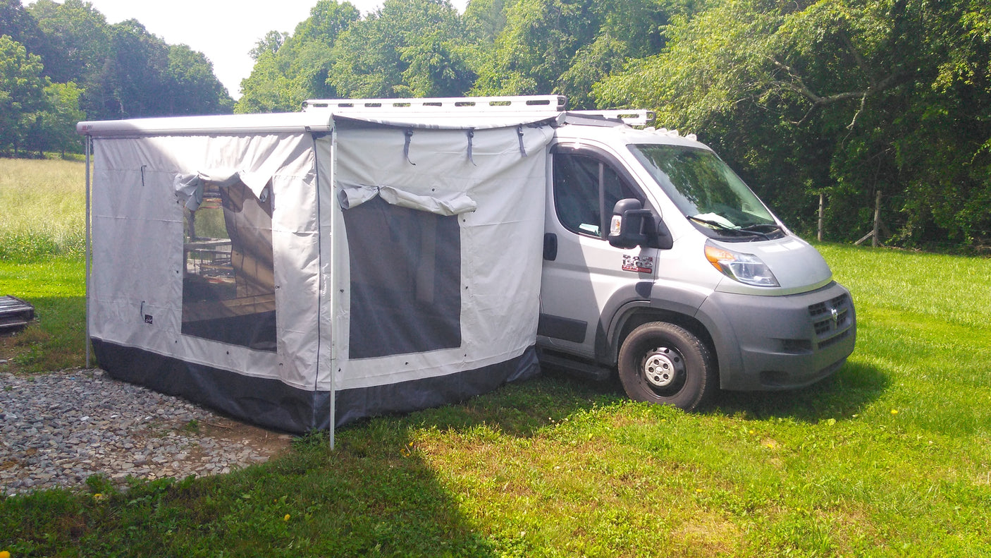 RV rental with expanded outdoor living. This campervan features a large grey awning tent, parked on grass beside gravel.