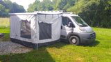 RV rental with expanded outdoor living. This campervan features a large grey awning tent, parked on grass beside gravel.
