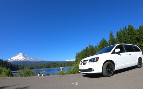 A white minivan parked by a scenic lake with a snow-capped mountain backdrop. An ideal spot for your RV rental journey to enjoy outdoor recreation.