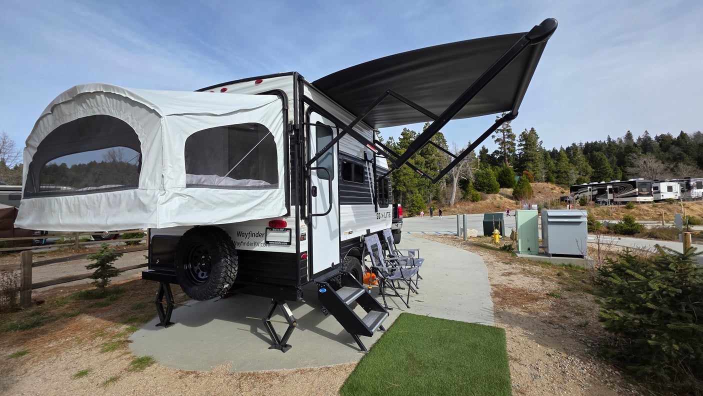 A Wayfinder rv rental travel trailer, with a pop-out tent bed and awning, set up in a scenic RV park.
