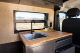 Inside an RV rental: a modern camper van kitchen with a sink, bamboo countertop, and a picturesque mountain view from the window.