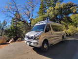 A silver Mercedes Sprinter rv rental, a Class B camper van, parked on an autumn road with vibrant trees & large rocks.