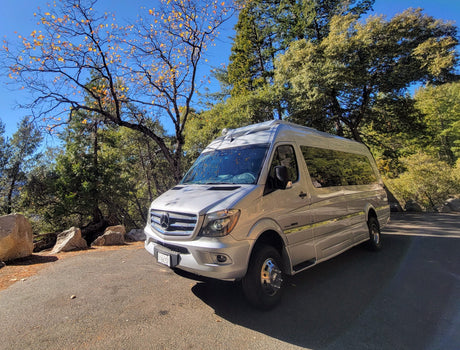 A silver Mercedes Sprinter rv rental, a Class B camper van, parked on an autumn road with vibrant trees & large rocks.
