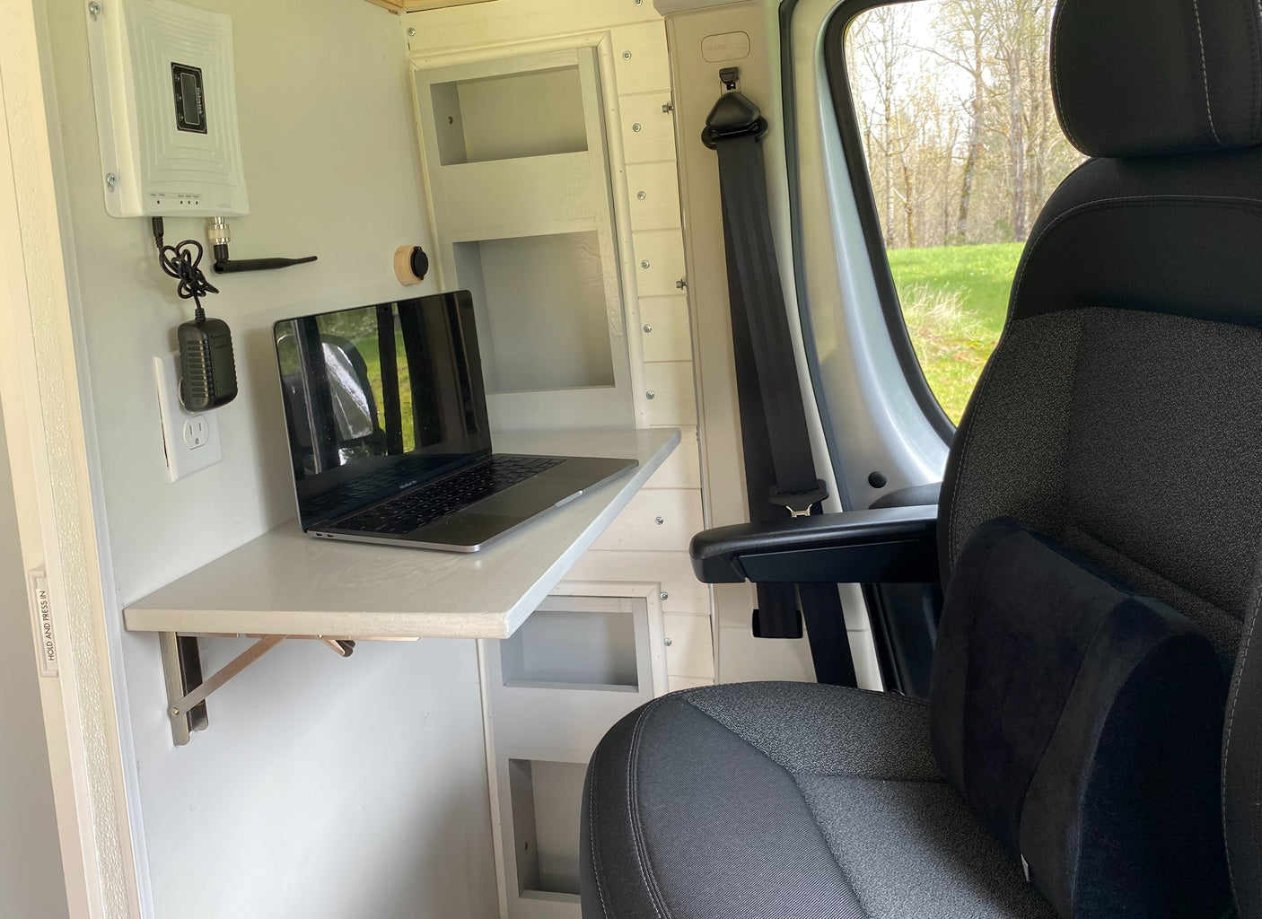 RV rental mobile office: MacBook on a fold-down desk with a cell booster, comfortable seat, and nature views outside.