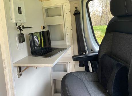RV rental mobile office: MacBook on a fold-down desk with a cell booster, comfortable seat, and nature views outside.