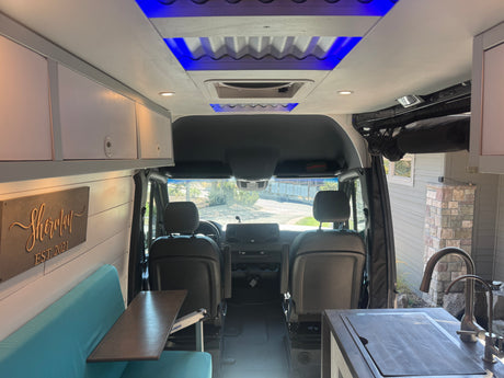 Spacious RV rental camper van interior. Features include a teal dinette, kitchen, and unique blue ceiling lights.