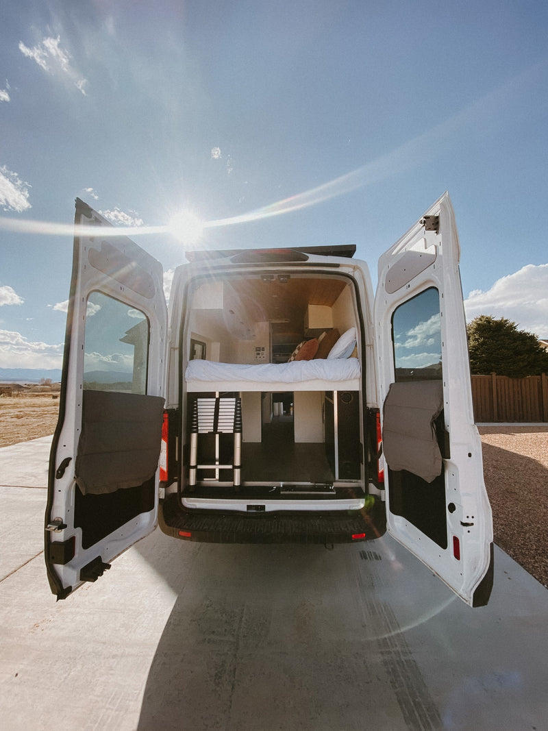 Sun-drenched white camper van, ideal RV rental. Rear doors open to reveal a cozy bed & storage, ready for van life adventures. — photo 7
