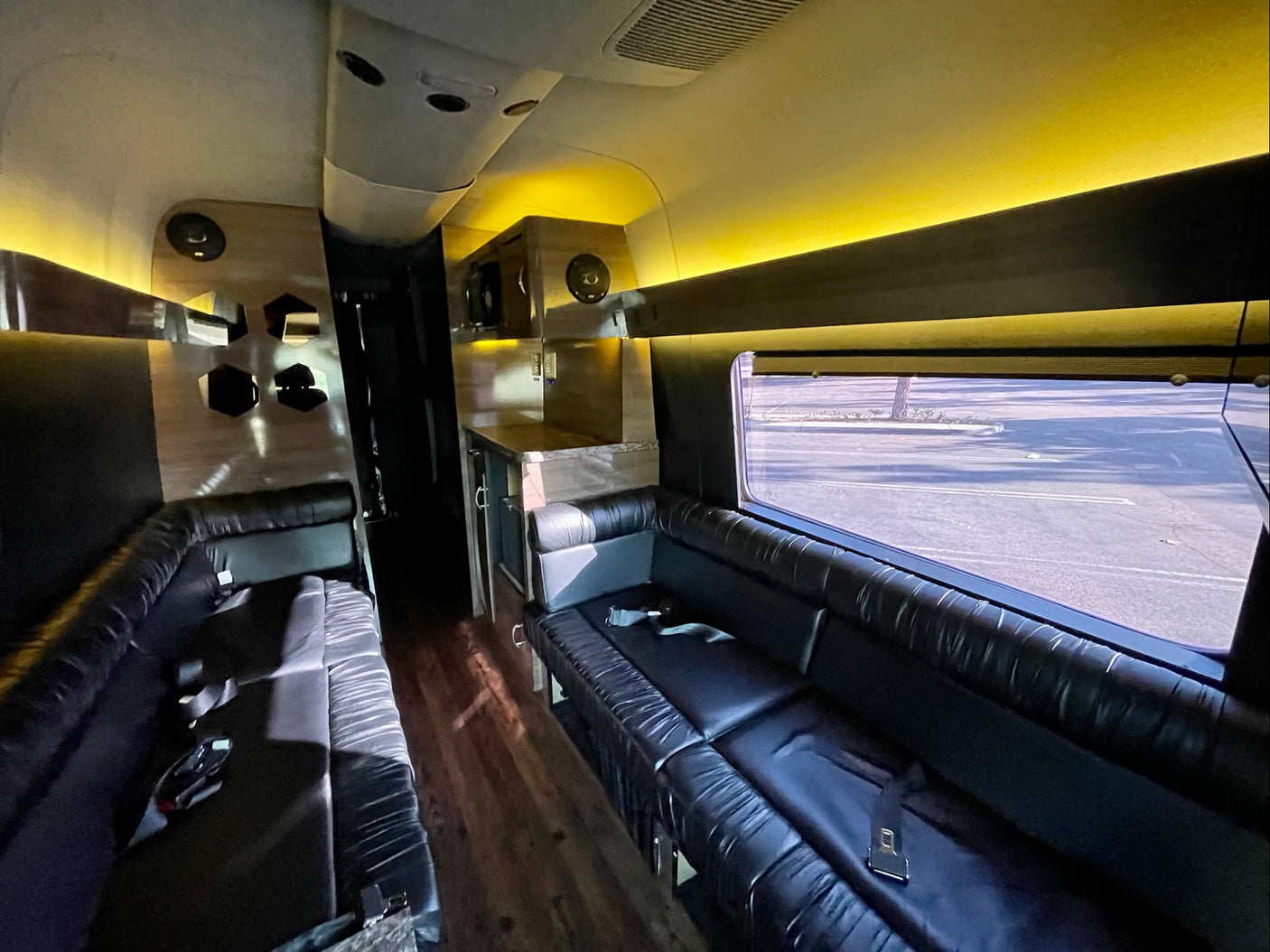 Inside a premium RV rental: plush black leather seating, a compact kitchenette, and warm overhead lighting set for comfort.