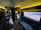 Inside a premium RV rental: plush black leather seating, a compact kitchenette, and warm overhead lighting set for comfort.