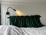 Cozy RV rental bedroom: white beadboard wall, reading lamp, and dark green velvet valance over a comfortable bed.