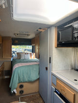 Cozy RV rental interior featuring a teal-covered bed and compact kitchen space, ideal for road trip adventures.