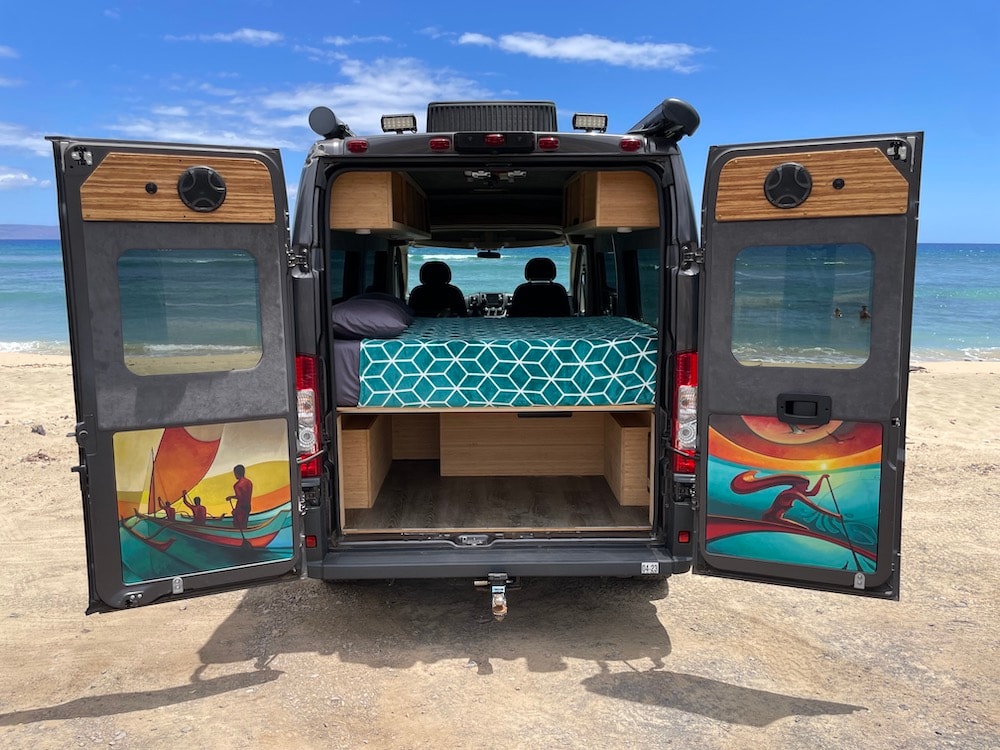 This RV rental is parked on a beach with its back doors open