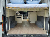 Spacious camper van interior, ideal for RV rental. Raised bed, under-bed storage, and compact kitchen offer comfortable mobile living.