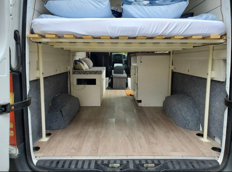 Spacious camper van interior, ideal for RV rental. Raised bed, under-bed storage, and compact kitchen offer comfortable mobile living. — photo 6