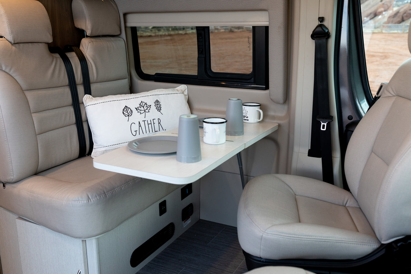 An RV rental's inviting interior with a table set for two, plush seating, and a window revealing a desert landscape.