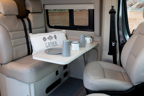 An RV rental's inviting interior with a table set for two, plush seating, and a window revealing a desert landscape.