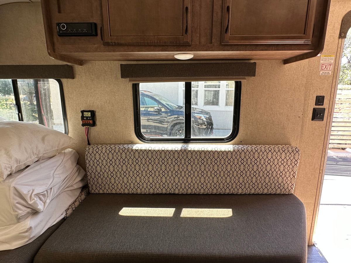 RV rental interior with a comfortable bed/seating area, overhead cabinets, and entertainment system. Solar controller and window view visible. — photo 7