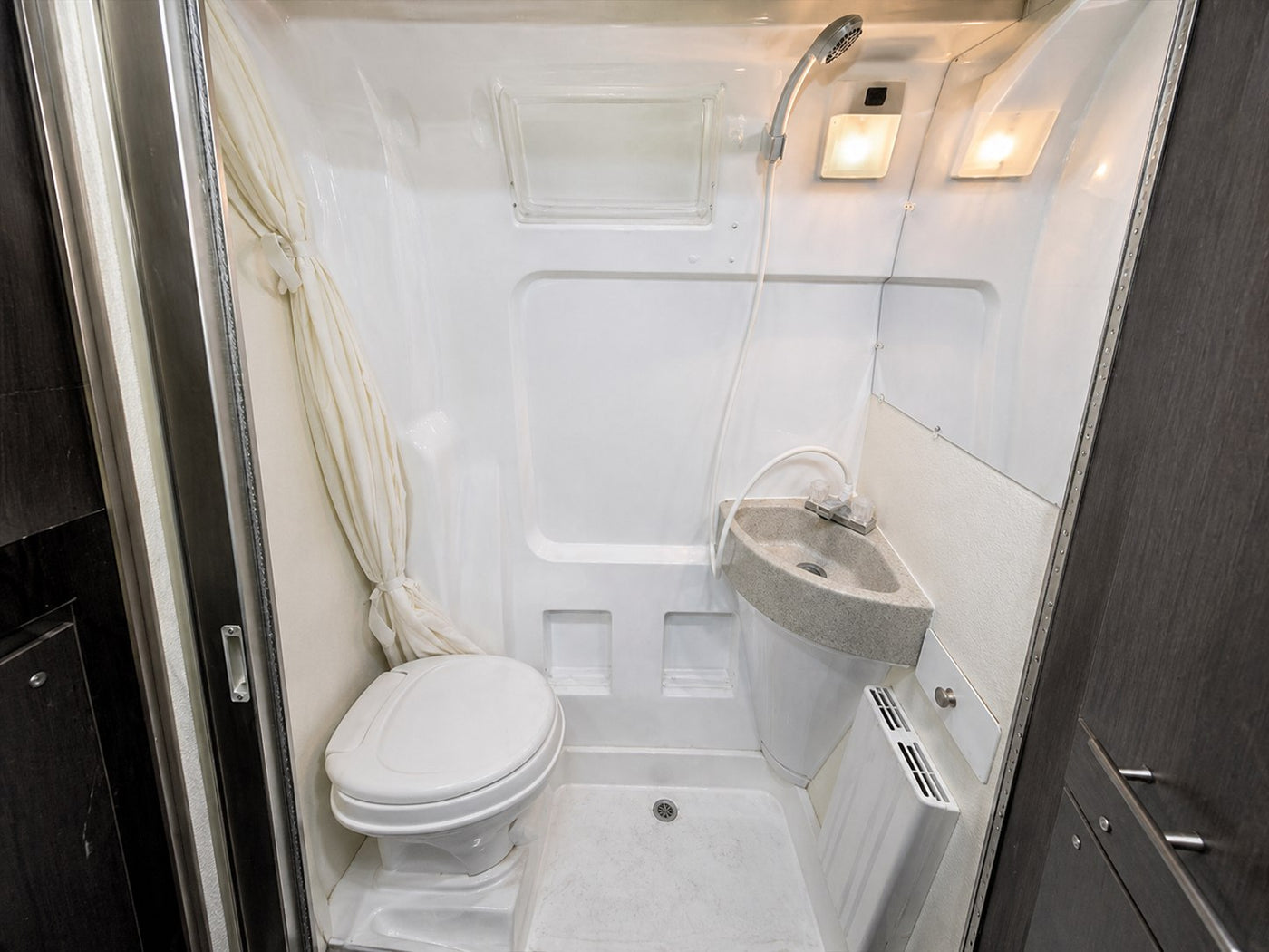 Compact RV rental bathroom with a white toilet, corner sink, and shower, perfect for small living spaces. — photo 10