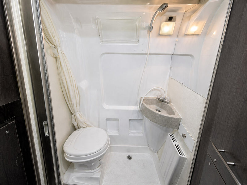 Compact RV rental bathroom with a white toilet, corner sink, and shower, perfect for small living spaces. — photo 10