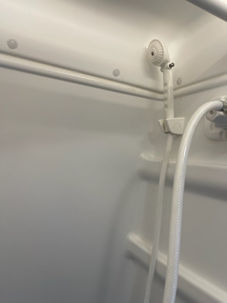 White shower head & hose in a compact rv rental bathroom, ideal for road trips & adventure.