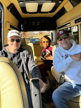 Smiles all around inside a premium **RV rental**! Three friends enjoy a sunny day trip, ready for fun with a football in their luxury travel van.