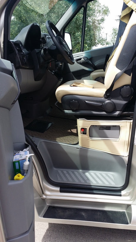 Inside an rv rental van: driver's area with tan seat, steering wheel, open door. Sanitizer in door pocket, control unit below seat.