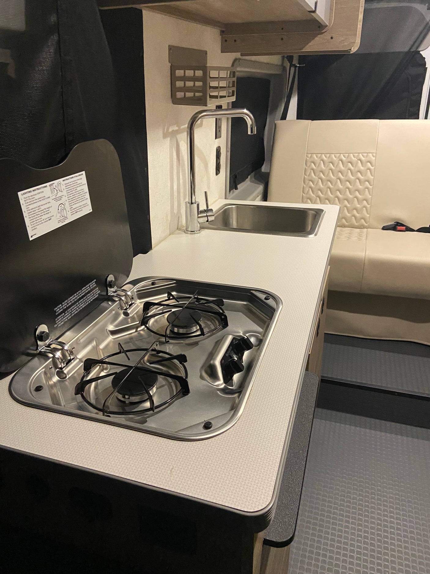 RV rental kitchen area: 2-burner stove, sink, and comfy seating inside a camper van.