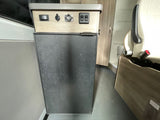 This RV rental features a compact refrigerator. Above it, a control panel with a toggle switch, 12V, USB ports, and other switches.