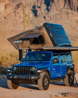 This blue Jeep Wrangler, equipped with a Desert Armor rooftop tent, offers an ideal RV rental for desert adventures.