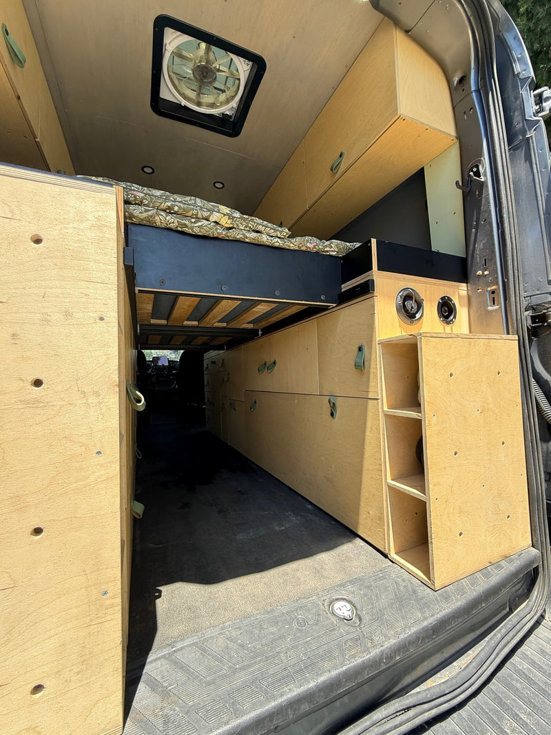 RV rental ready: custom camper van interior featuring a raised bed, plywood storage cabinets, and a ceiling fan. — photo 6