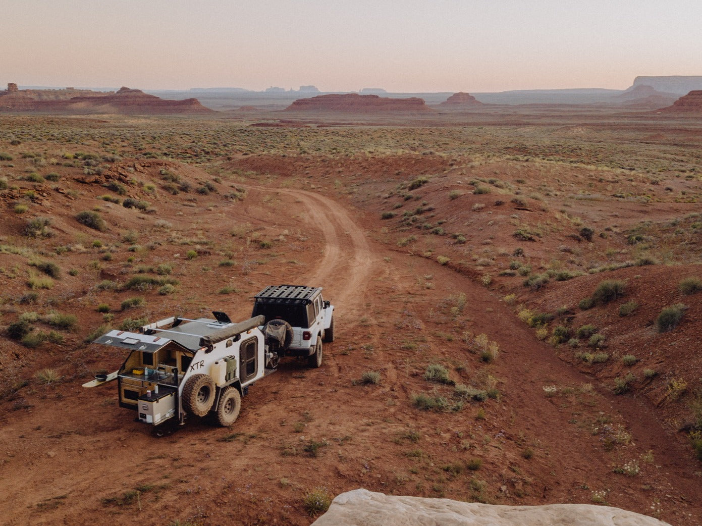 Explore the desert! This white Jeep pulls an off-road RV rental, its rear kitchen open for remote adventure camping.