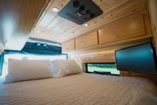 A comfortable RV rental interior with a bed, overhead storage, and TV, perfect for travel.