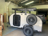 This tear-drop camping trailer, an ideal RV rental, boasts a sturdy roof rack and rear-mounted spare tire.