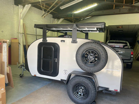 This tear-drop camping trailer, an ideal RV rental, boasts a sturdy roof rack and rear-mounted spare tire.