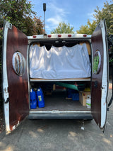 Open rear of an RV rental camper van, revealing a bed, water jugs, and gear storage for an adventurous mobile setup.
