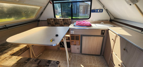 Cozy A-frame RV rental interior, featuring a dining area with table and benches, and a compact kitchenette with sink, stove, and fridge.
