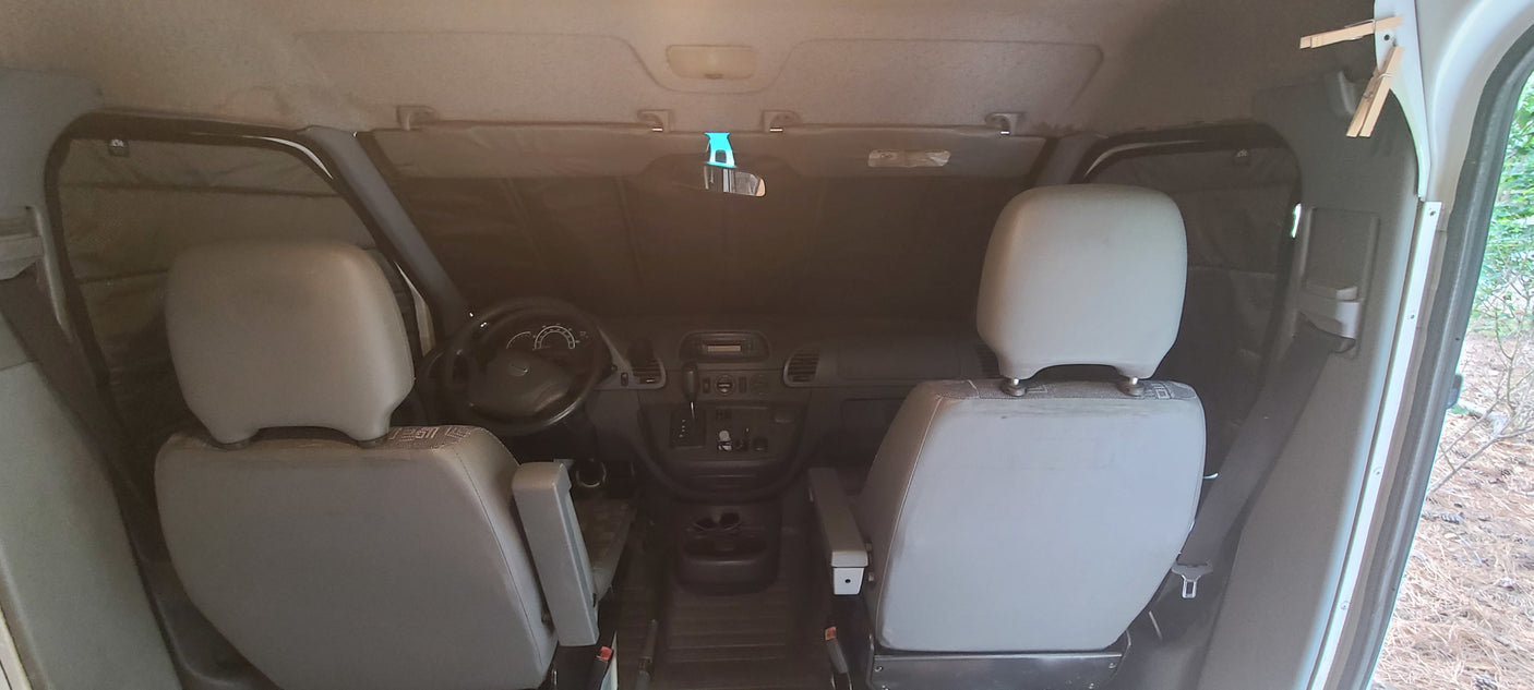 View inside an RV rental's front cabin, showing seats, steering wheel, and window coverings for privacy and insulation.