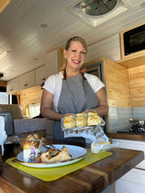 Smiling woman holds fresh biscuits in an RV rental kitchen. Perfect for cozy travels and delicious meals.