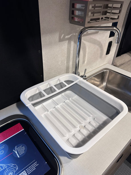Compact RV rental kitchen with a stainless steel sink, chrome faucet, and collapsible dish drying rack.