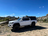 A white Toyota Tacoma with a truck bed camper parked in a scenic rocky landscape, ideal for an RV rental adventure.