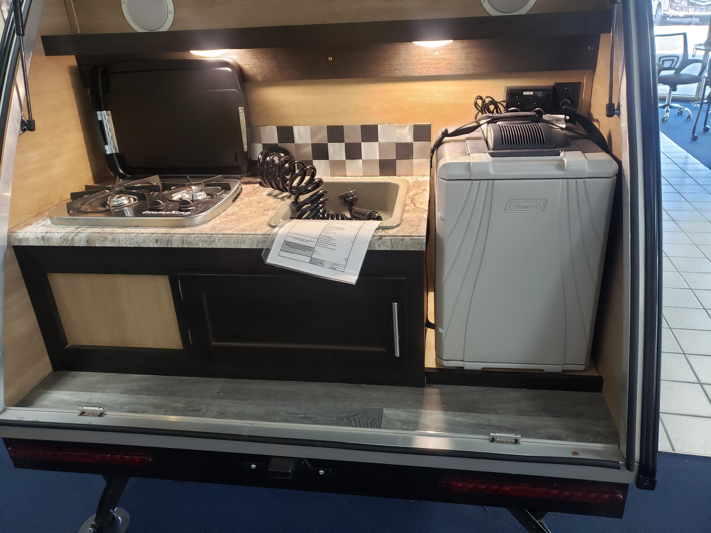 This compact RV rental's rear galley reveals a two-burner stove, sink, and Coleman cooler for outdoor cooking and camping trips.