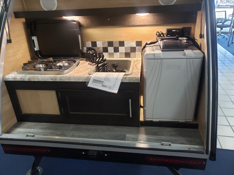 This compact RV rental's rear galley reveals a two-burner stove, sink, and Coleman cooler for outdoor cooking and camping trips. — photo 6