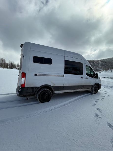 Experience winter adventures in this rugged RV rental camper van, parked in fresh snow with tire tracks and footprints.
